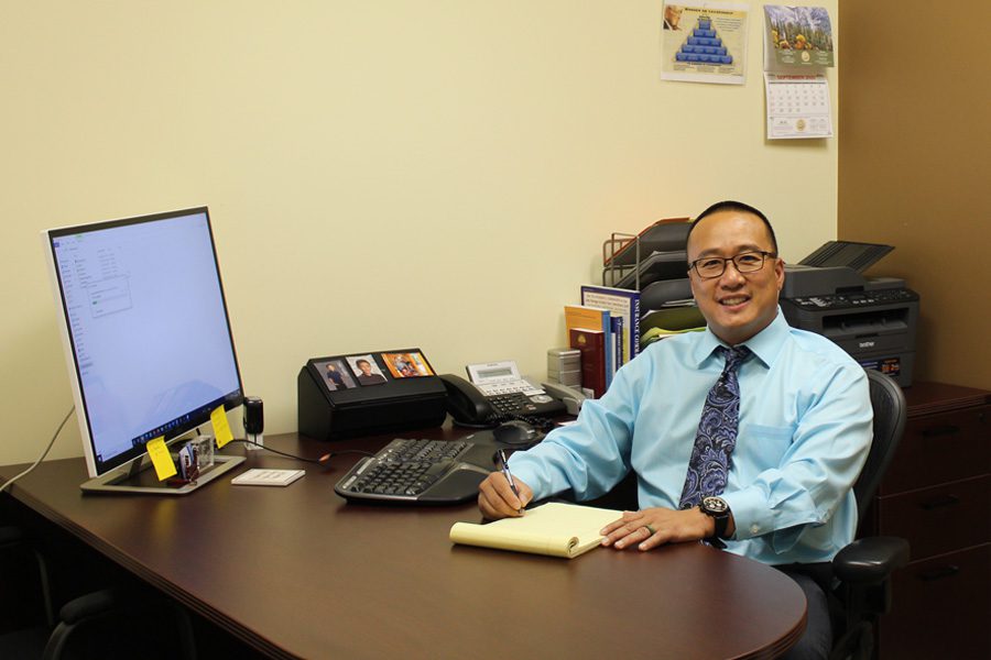 About Our Agency - Portrait of MKC Insurance Services Owner Mike Chan Sitting in His Office Working on the Computer and Using a Writing Notes on a Notepad