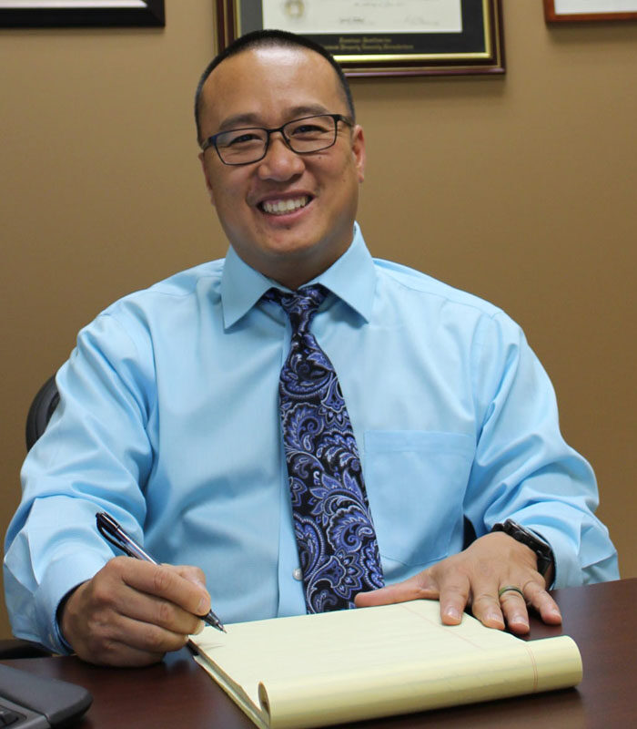 About Our Agency - Portrait of MKC Insurance Services Owner Mike Chan Sitting in His Office Working on the Computer and Using a Writing Notes on a Notepad